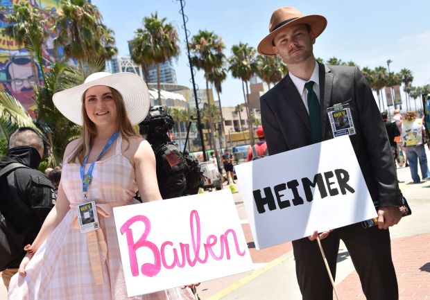 Cosplayers hold Barbenheimer signs outside the convention center during San Diego Comic-Con International in San Diego, California, on July 21, 2023. (Photo by Chris Delmas / AFP) (Photo by CHRIS DELMAS/AFP via Getty Images)